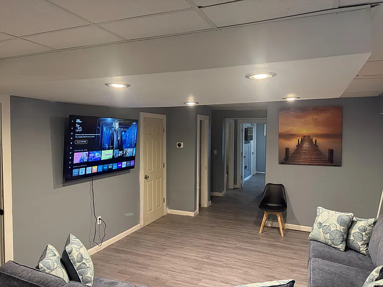 Open common lounge with durable plank flooring, recessed lighting, wall-mounted TV, and easy access to nearby rooms.