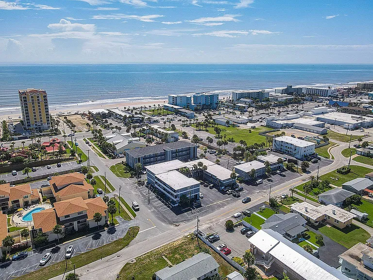 Breathtaking aerial view of vibrant coastal community featuring modern apartments, palm-tree lined streets, and sparkling ocean backdrop.