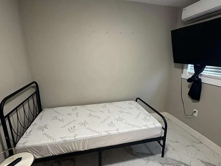Private bedroom with tiled flooring, window with blinds, wall-mounted TV, and efficient mini-split A/C for comfort.