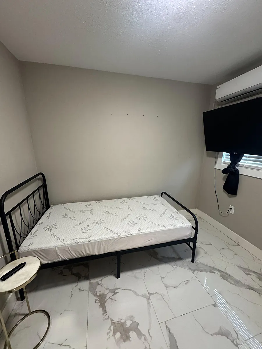 Private bedroom with tiled flooring, window with blinds, wall-mounted TV, and efficient mini-split A/C for comfort. - N 13th St