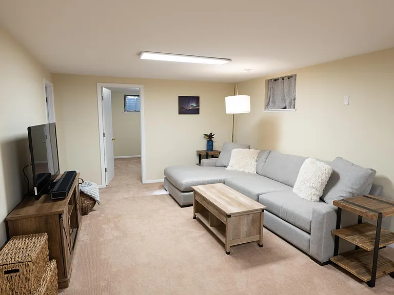 View from the stairs down to the finished half of the basement, showing the entrance to the additional room ahead and on the left, the path towards the exercise room.