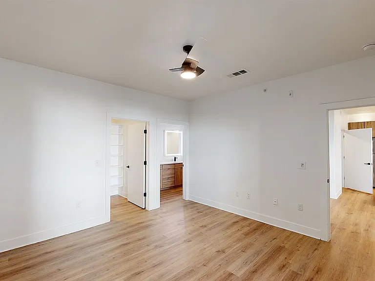 Spacious apartment bedroom with large closet, attached bathroom and wood-style flooring.