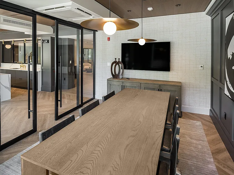 Elegant dining and conference room with a modern wooden table, stylish pendant lighting, and floor-to-ceiling glass doors leading to a sleek kitchen area at Parkside Place in Cambridge MA