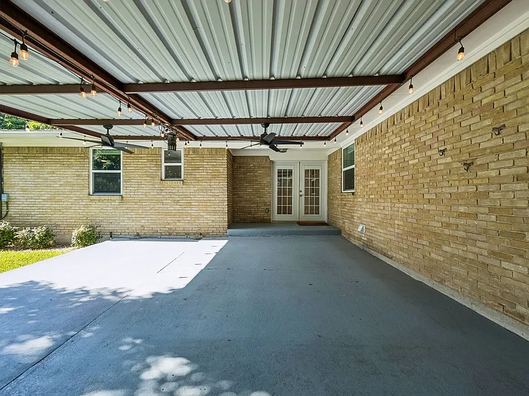 Expansive covered patio featuring a corrugated metal roof, string lighting, and ceiling fans