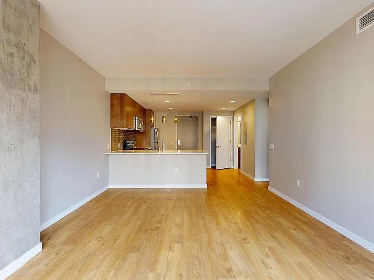 Apartment kitchen with stainless steel appliances, dining and living room with wood-style flooring.