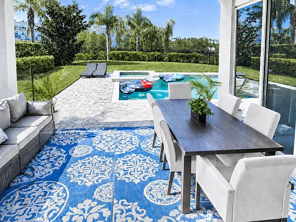 Covered patio with dining seating and lounge area, opening to a paved pool deck and landscaped backyard.
