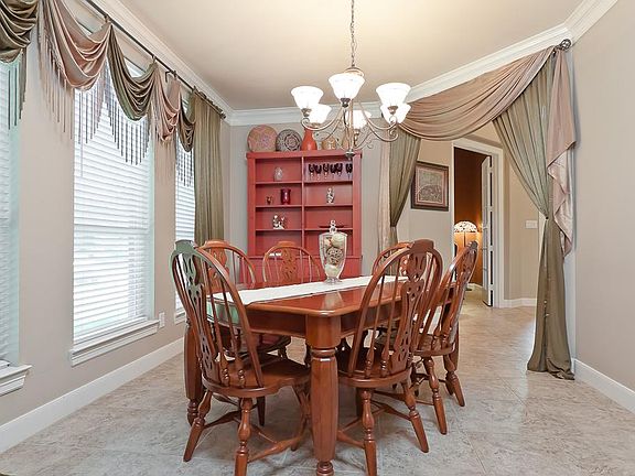 The formal dining room includes ceramic tile floors, crown moulding, a beautiful chandelier and a wall of windows with blinds and custom window treatments.