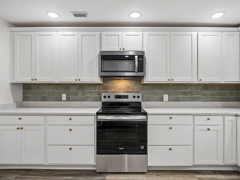 Kitchen featuring white cabinetry, light-toned countertops, a full suite of stainless steel appliances, a green subway tile backsplash, and recessed ceiling lighting
