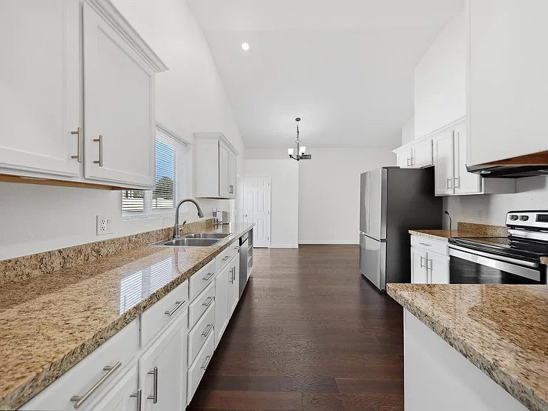 Galley kitchen with granite countertops, ample white cabinetry, double-basin sink, and stainless steel appliances.