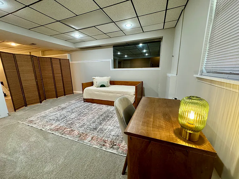 This spacious and temperature-controlled basement offers a flexible and functional living space. A twin daybed provides a comfortable spot for guests or daytime relaxation, while a designated workspace area is ideal for studying or working from home.
