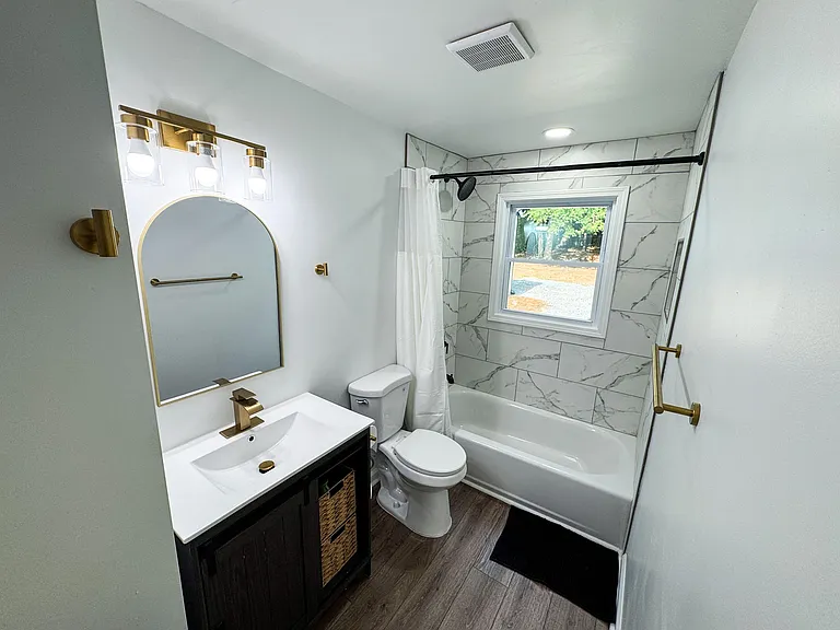 Updated full bath with tub/shower, tiled surround, and a vanity with storage plus a window for ventilation.