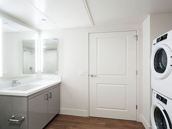 Bathroom with full-sized front loading washer dryer, backlit mirror and stunning vanities