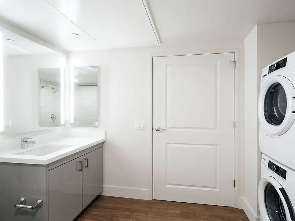 Bathroom with full-sized front loading washer dryer, backlit mirror and stunning vanities