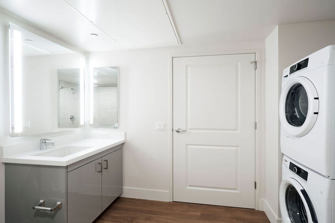 Bathroom with full-sized front loading washer dryer, backlit mirror and stunning vanities