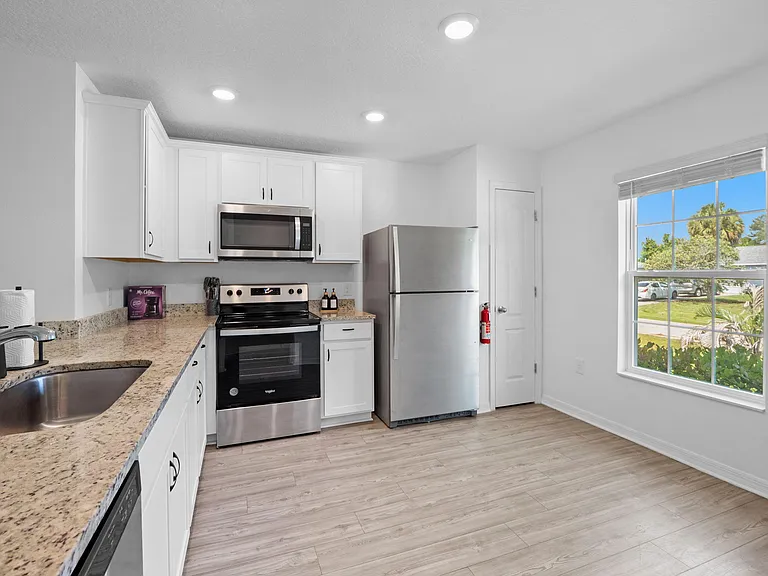 Efficient kitchen with granite-look counters, ample white cabinetry, and stainless steel appliances plus a large window.