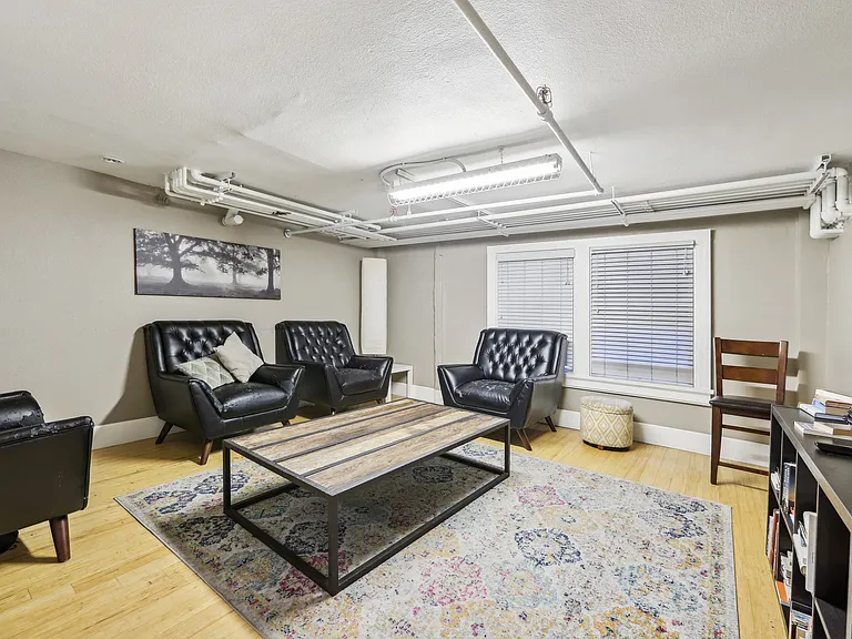 Room with a wooden coffee table surrounded with armchairs, bookshelf, and a flat-screen TV