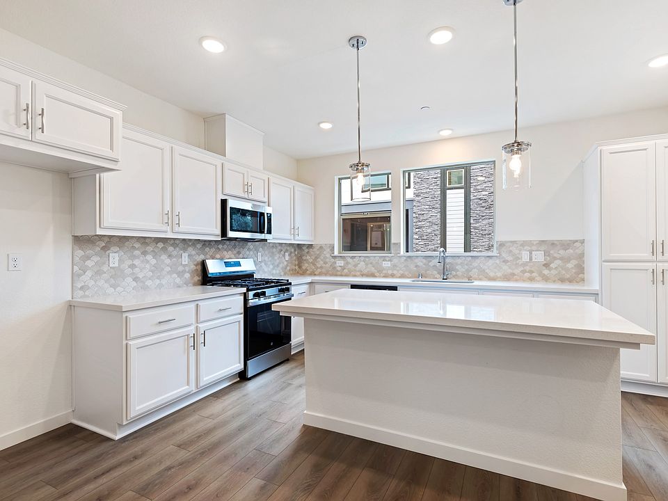 A modern, well-lit kitchen with white cabinets, a stone backsplash, and hardwood floors, featuring a