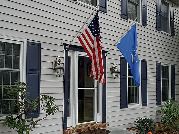 The colonial-style home has light gray siding with beefed up insulation, dark blue shutters, architectural shingle roofing, and custom triple pane windows.