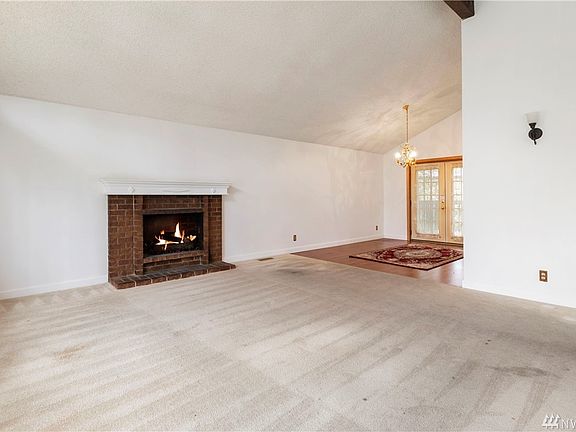 Spacious living room with vaulted ceiling and fireplace with brick surround and white mantle.