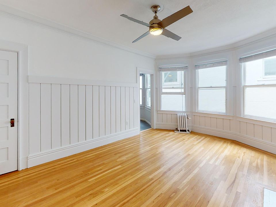 Bright room with hardwood floors, paneling, a ceiling fan, and large windows providing natural light