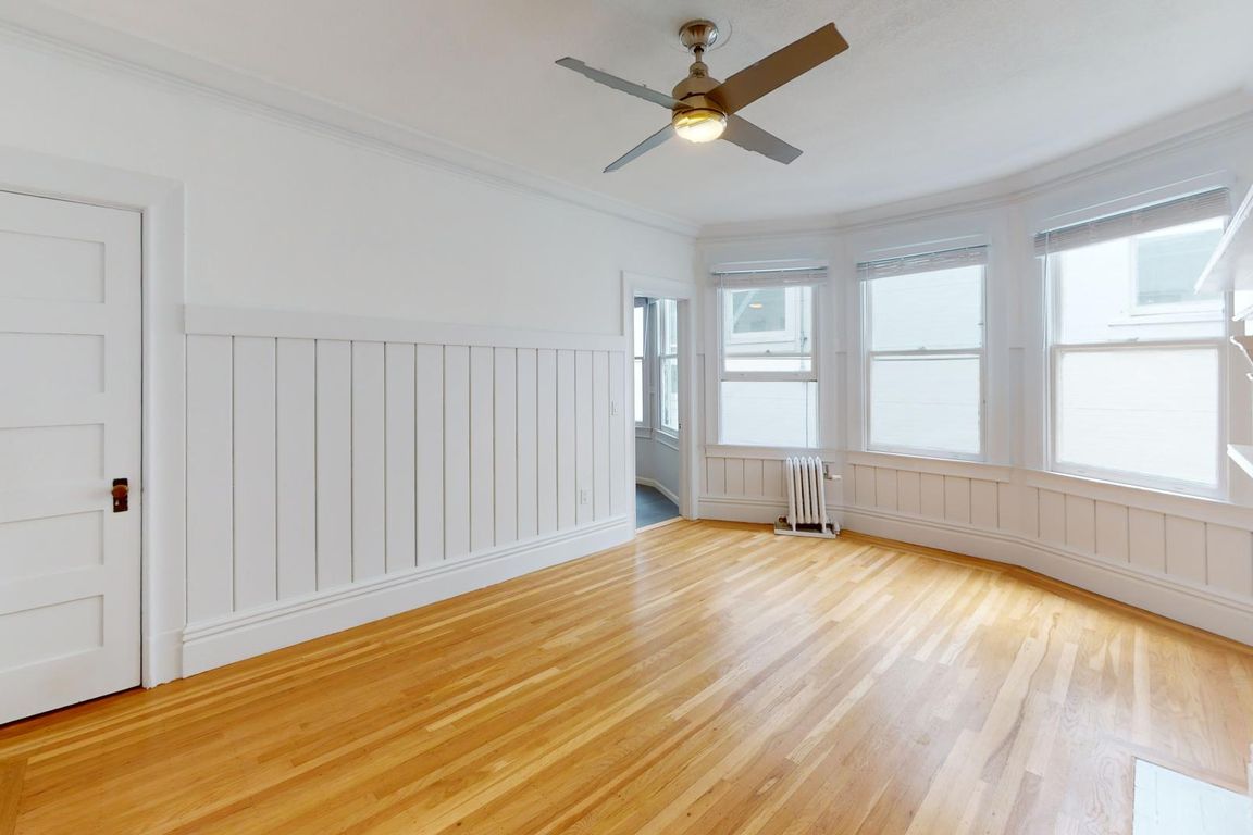 Bright room with hardwood floors, paneling, a ceiling fan, and large windows providing natural light