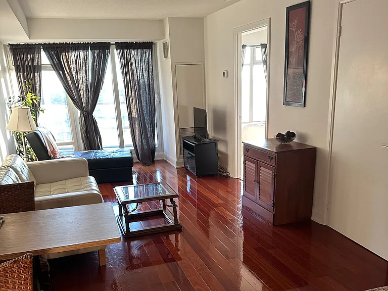 Living room shown from behind kitchen counter looking out. Bedroom door at right back. Smart TV and console in right corner. Wifi included in monthly rental cost