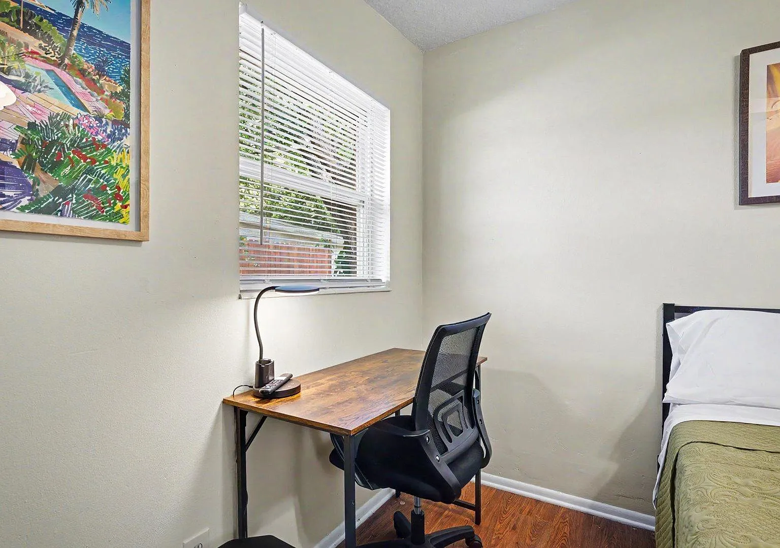 Dedicated work desk, chair & lamp, window with blinds, and and attractive artwork.