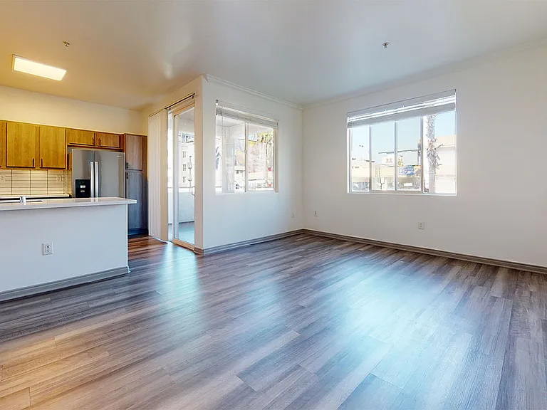 Apartment kitchen with stainless steel appliances, dining and living room with wood-style flooring.