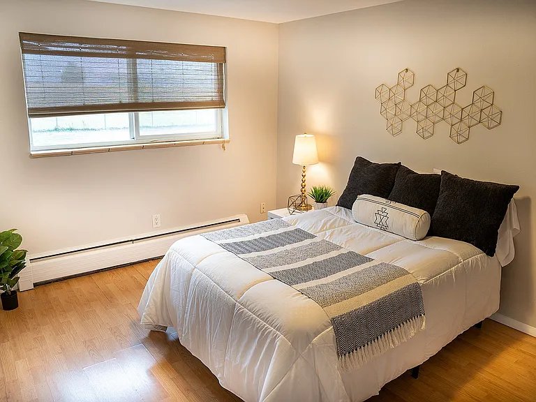 Inviting bedroom featuring a cozy bed with plush pillows, natural light streaming through window blinds, and elegant decor on the walls. Perfect for relaxation and comfort.