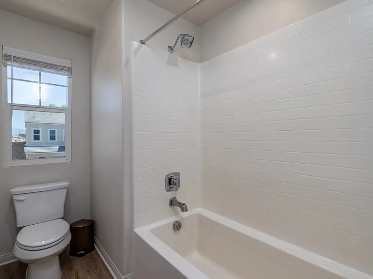 Bright upstairs shared bathroom featuring a modern shower-tub combo with clean white tile surround, stylish fixtures, and natural light from a large window_perfect for comfort and functionality in this contemporary Menifee home.