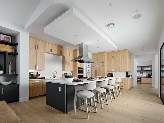 A modern, open-concept kitchen with light wood cabinetry, a large island with bar stools, and a slee