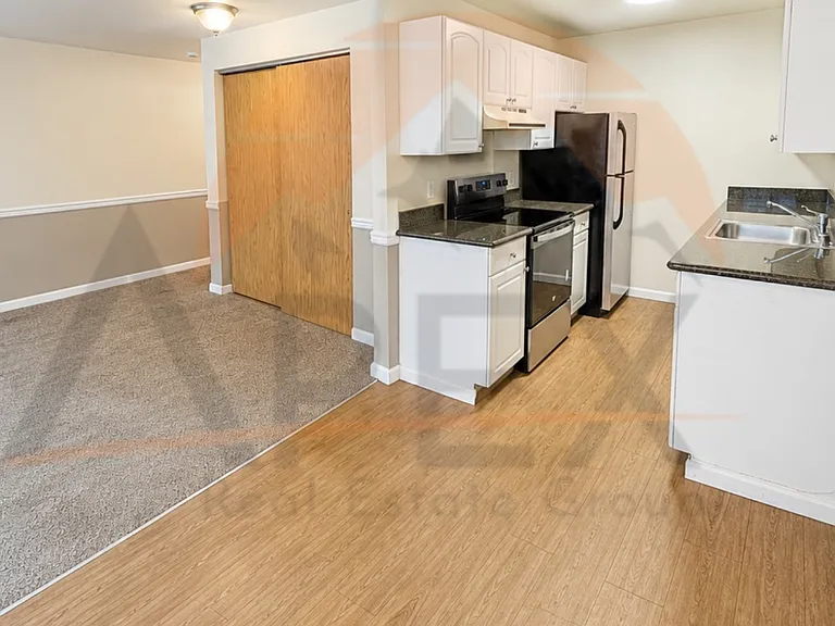 Well-lit kitchen area with wood-look flooring, white cabinetry, and full-size appliances.