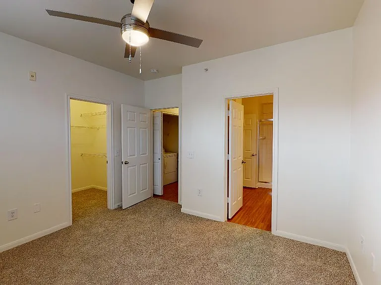 Spacious apartment bedroom with large closet, attached bathroom and plush carpet flooring.