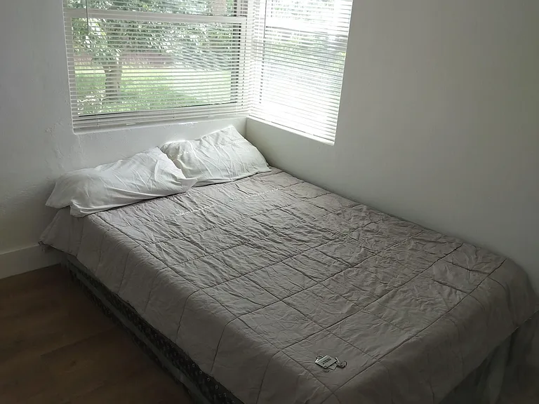 Bedroom with a comfortable bed and corner windows with blinds, offering a pleasant view and natural light.