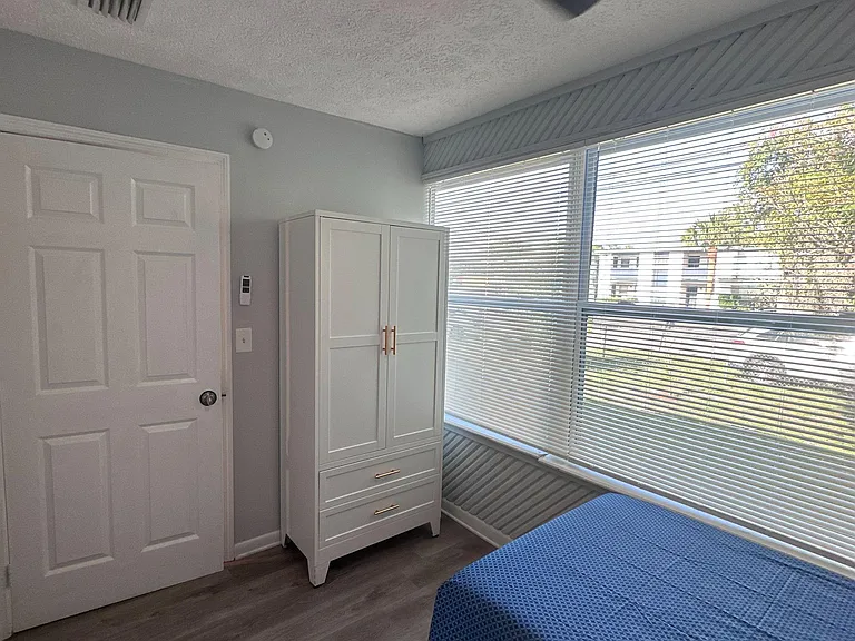 Furnished bedroom with a ceiling fan, wardrobe storage, and a large window with blinds for natural light.