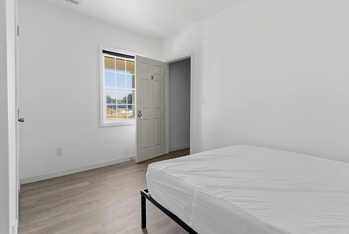 Private bedroom with wood-look flooring, a large window for natural light, and easy access to the hallway. - S South St