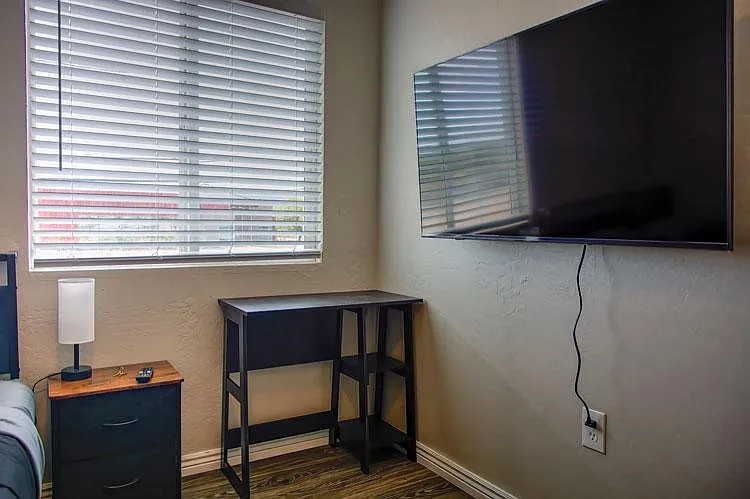 Bedroom area with window blinds, wall-mounted TV, and a small desk space for working or studying.