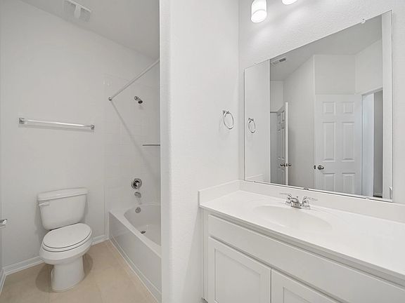The secondary bath features tile flooring, white cabinetry and light countertops and a shower tub co