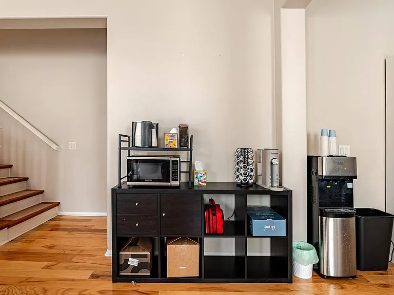 Common area nook with beverage station, microwave, and open cubby storage near the stairway for easy daily use.
