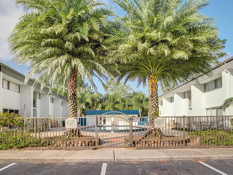 Inviting apartment complex entrance with lush palm trees and a gated path, offering a glimpse of vibrant, spacious living.