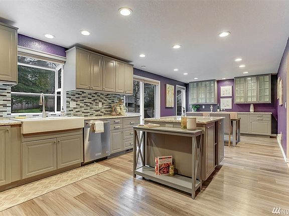 This bright remodeled kitchen features luxury laminate flooring, gray cabinets, glass tile back splash, farm house sink and large kitchen island with plenty of storage.