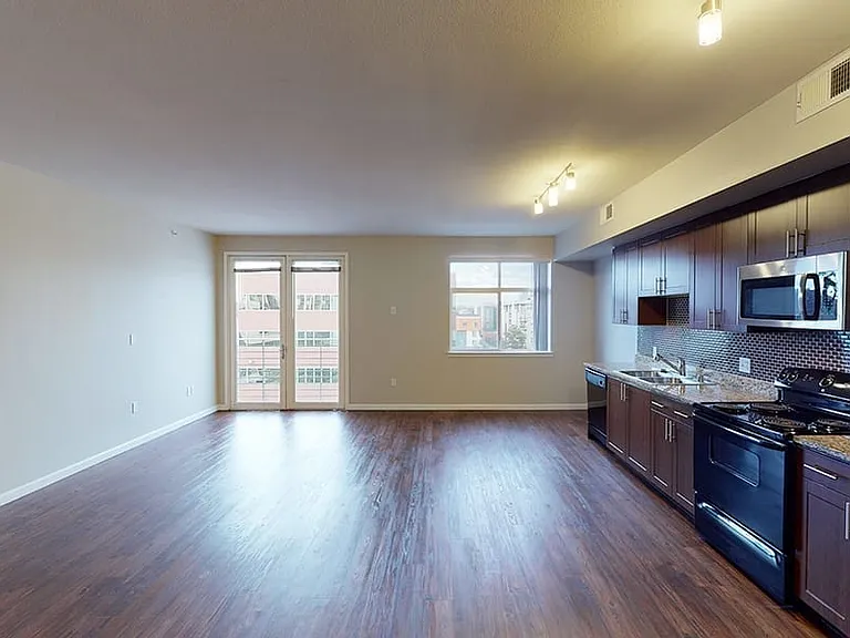 Apartment kitchen with stainless steel appliances, dining and living room with wood-style flooring and balcony or patio in select homes.