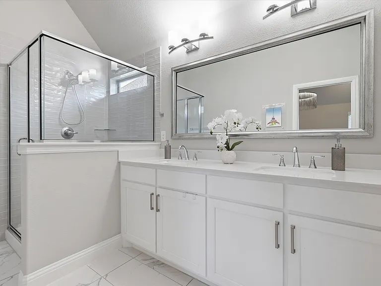 Primary bathroom with double vanity, white cabinetry, quartz-finish countertops, and a large walk-in closet.