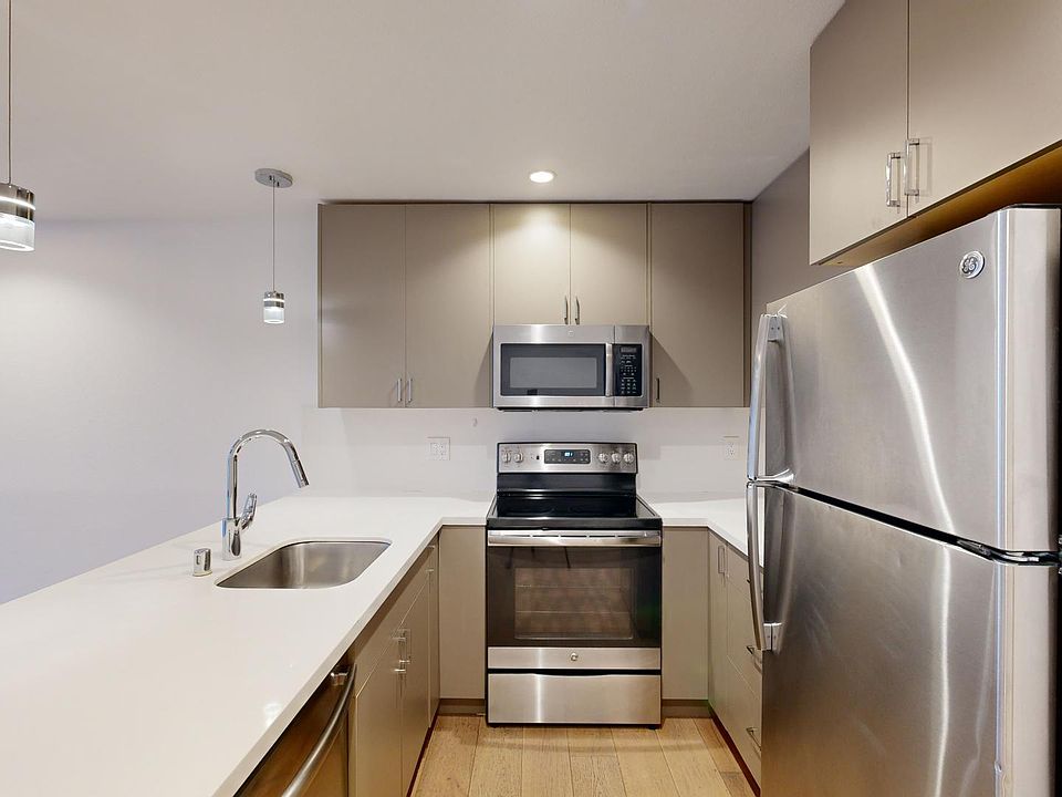 Modern kitchen with stainless steel appliances, including a refrigerator, oven, and microwave. Sleek countertops and pendant lighting create a clean, minimalist feel.