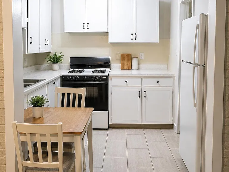 Efficient eat-in kitchen with white cabinetry, gas range, full-size refrigerator, and ample counter space for meal prep.