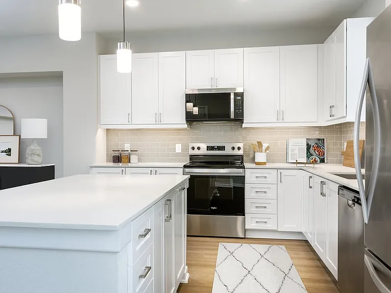 Finish Package I townhome kitchen with stainless steel appliances, white cabinetry, grey tile backsplash, white quartz countertops, and hard surface flooring