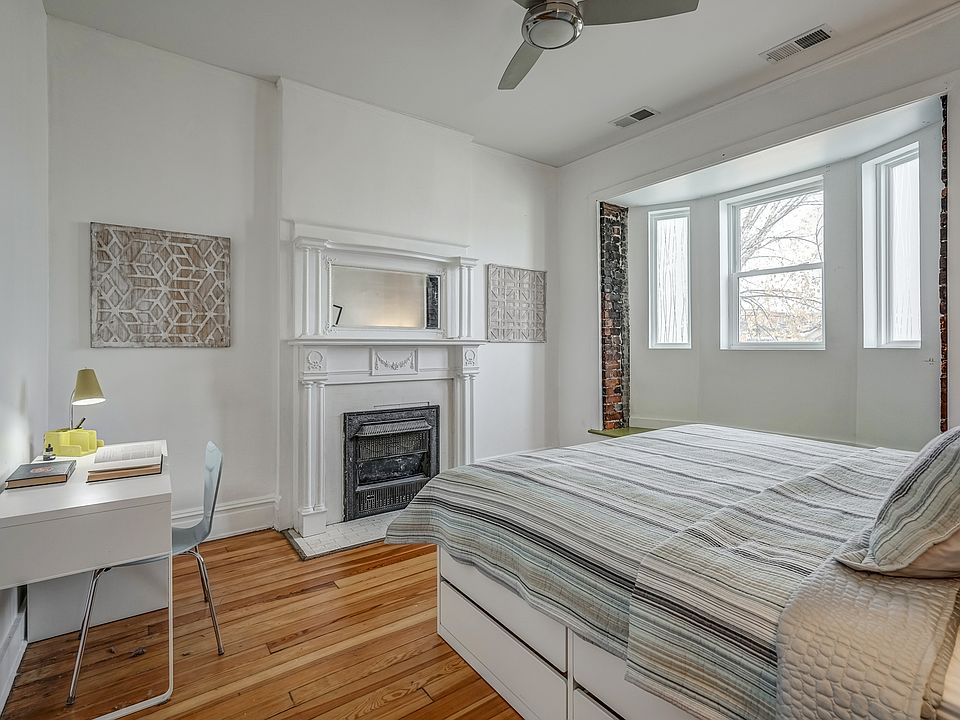 Huge primary bedroom with bay windows and windows seat, fireplace, desk, and ceiling fan.