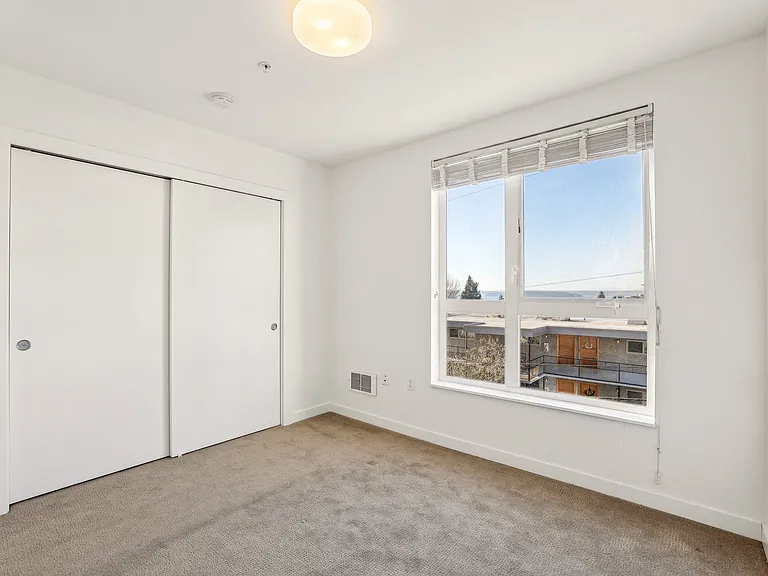 Spacious bedroom at 4400 Alaska in Seattle, WA, featuring comfortable light brown carpet, ample closet space, and a large window providing natural light and ...