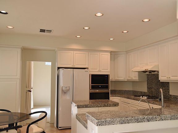 White shaker-style kitchen cabinets with granite countertops, eat-in dining space, built-in appliances, recessed lighting