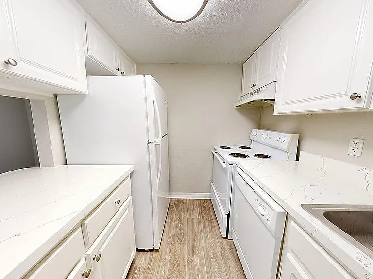 Modern kitchen with sleek white cabinetry, spacious countertops, and essential appliances including fridge and stove.